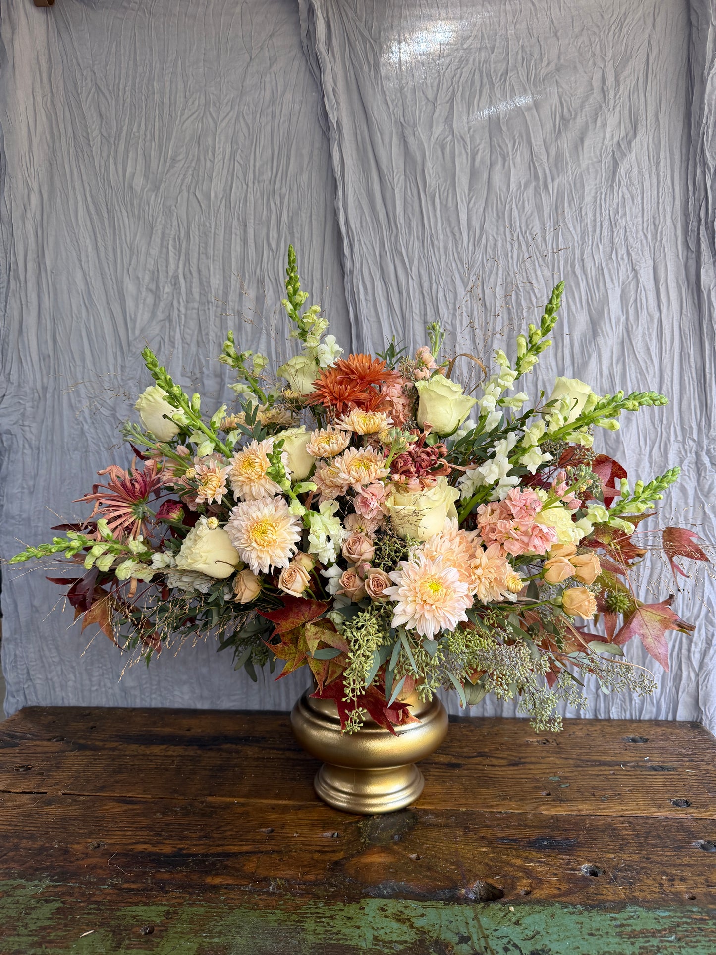 Floral arrangement with mums and snapdragons in a gold urn